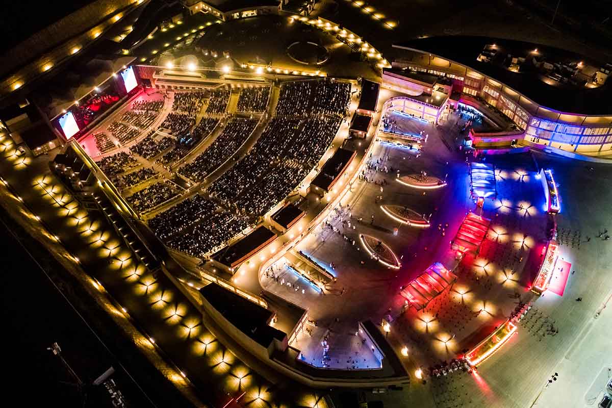 A birds-eye view of the Al Dana Amphitheatre taken at night showing the seating and staging all lit up.